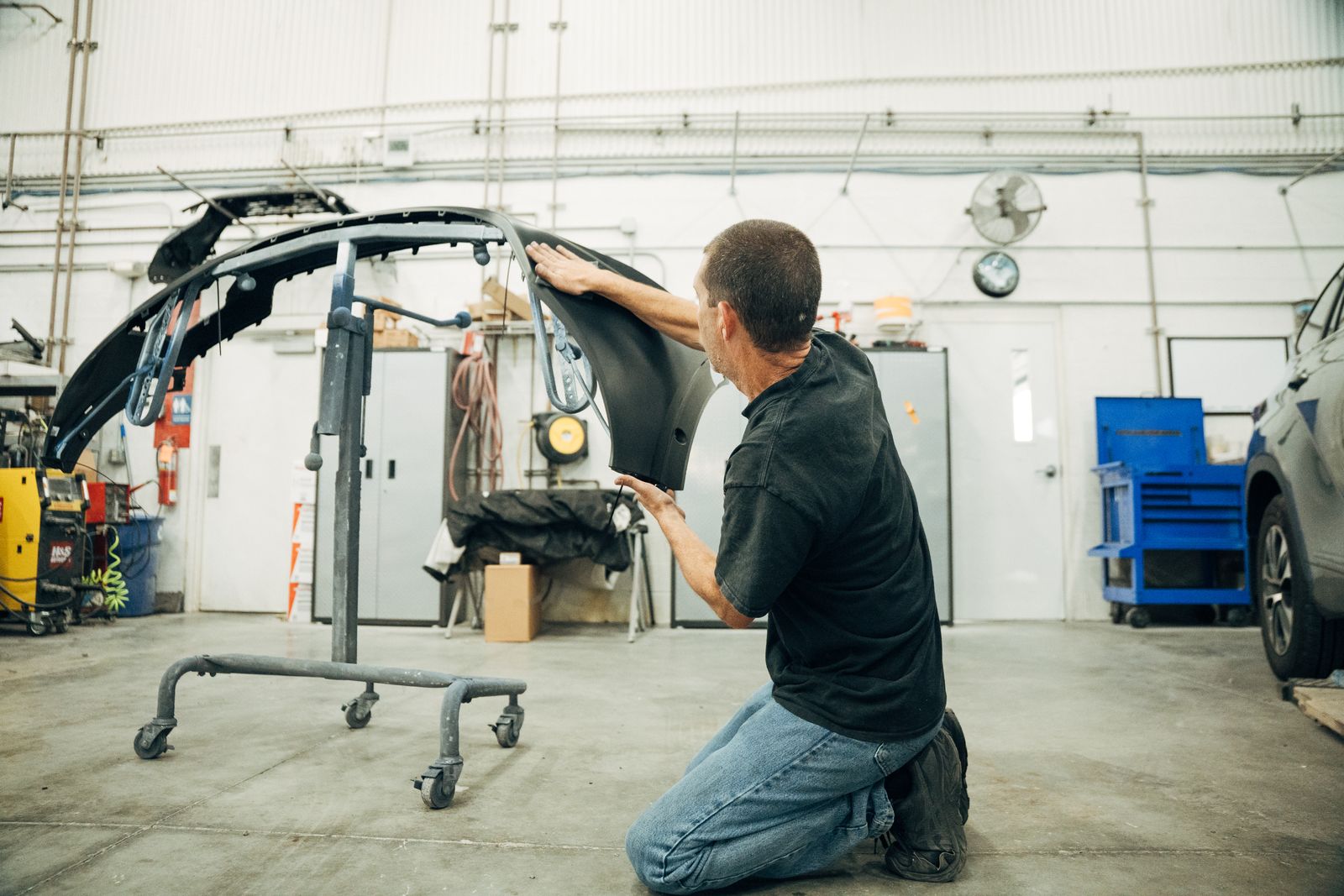 Technician fitting a front bumper cover in the shop