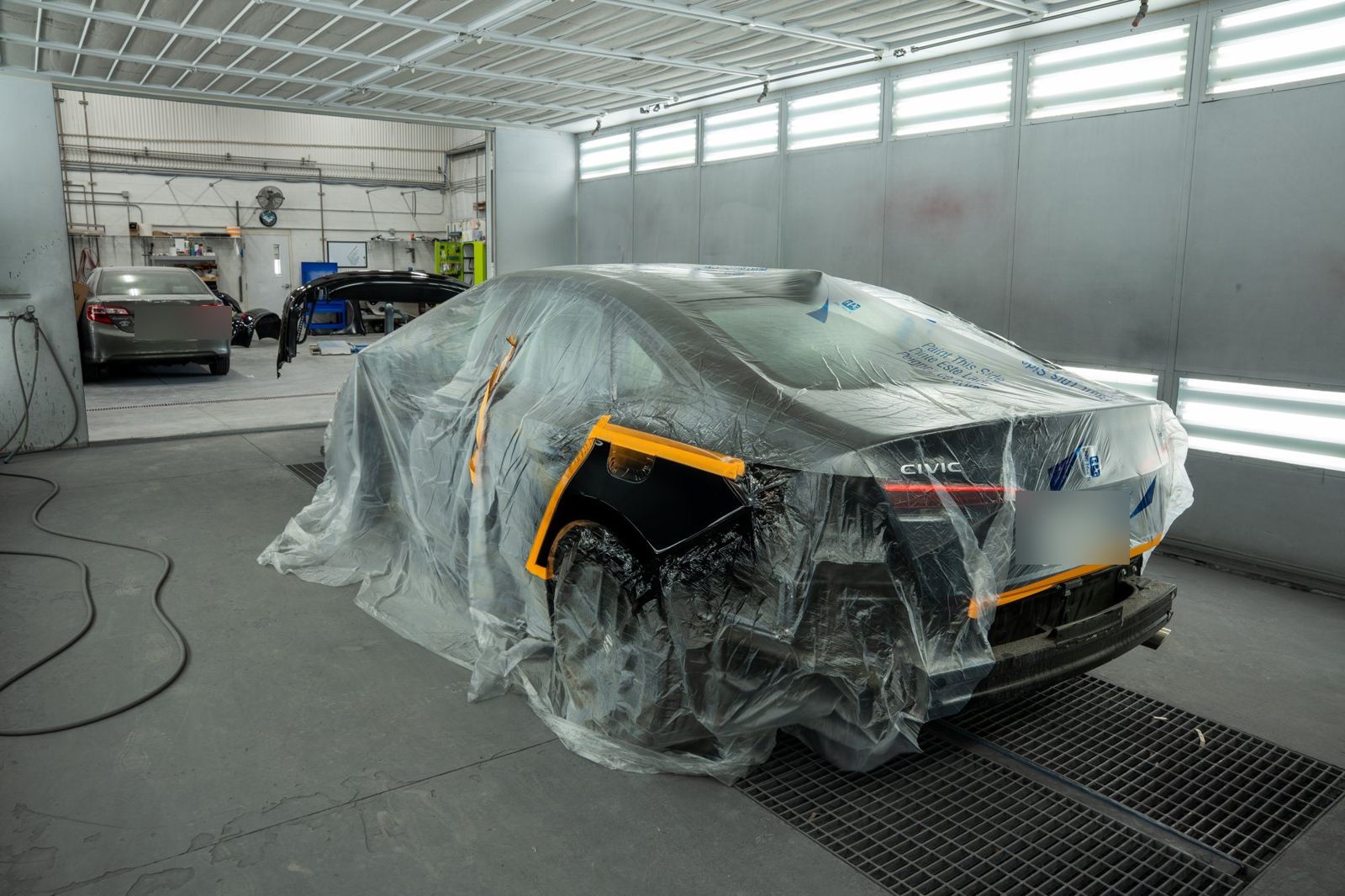 Honda Civic masked in plastic and tape in the paint booth