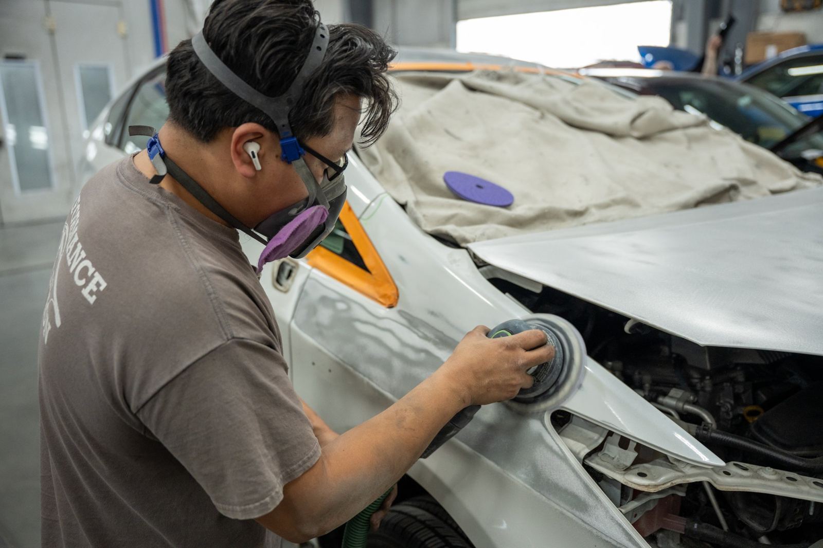 Technician in a respirator sanding a white fender before paint